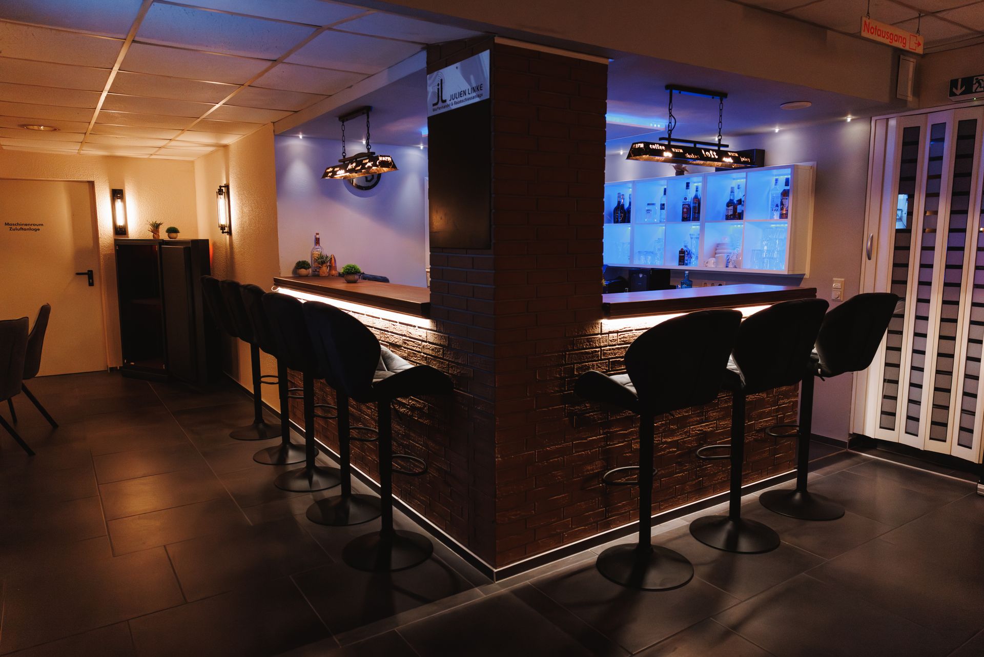 Bar der ApexLounge mit Barhockern und beleuchtetem Regal